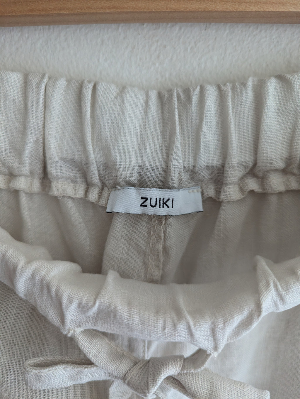 Close-up of a cream-colored textured fabric garment with a gathered elastic waistband and a white brand label reading 'ZUIKI'.